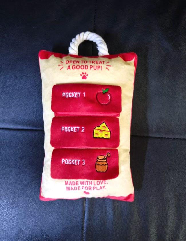 Finished treat-pocket activity pillow for dogs, cream and red, with three embroidered treat labels and a rope loop
